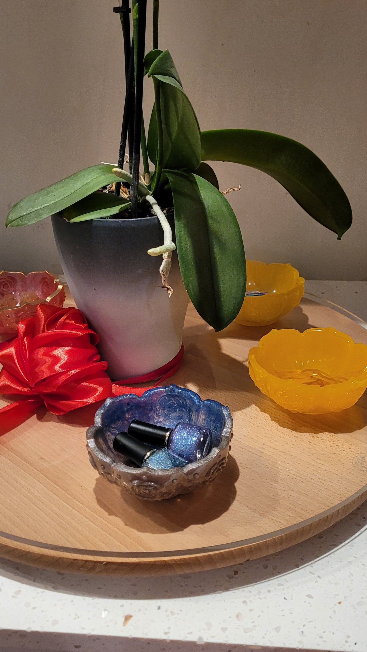 Decorative blue and silver flower-shaped  resin bowl, red ribbon, and other resin bowls on a wooden surface.