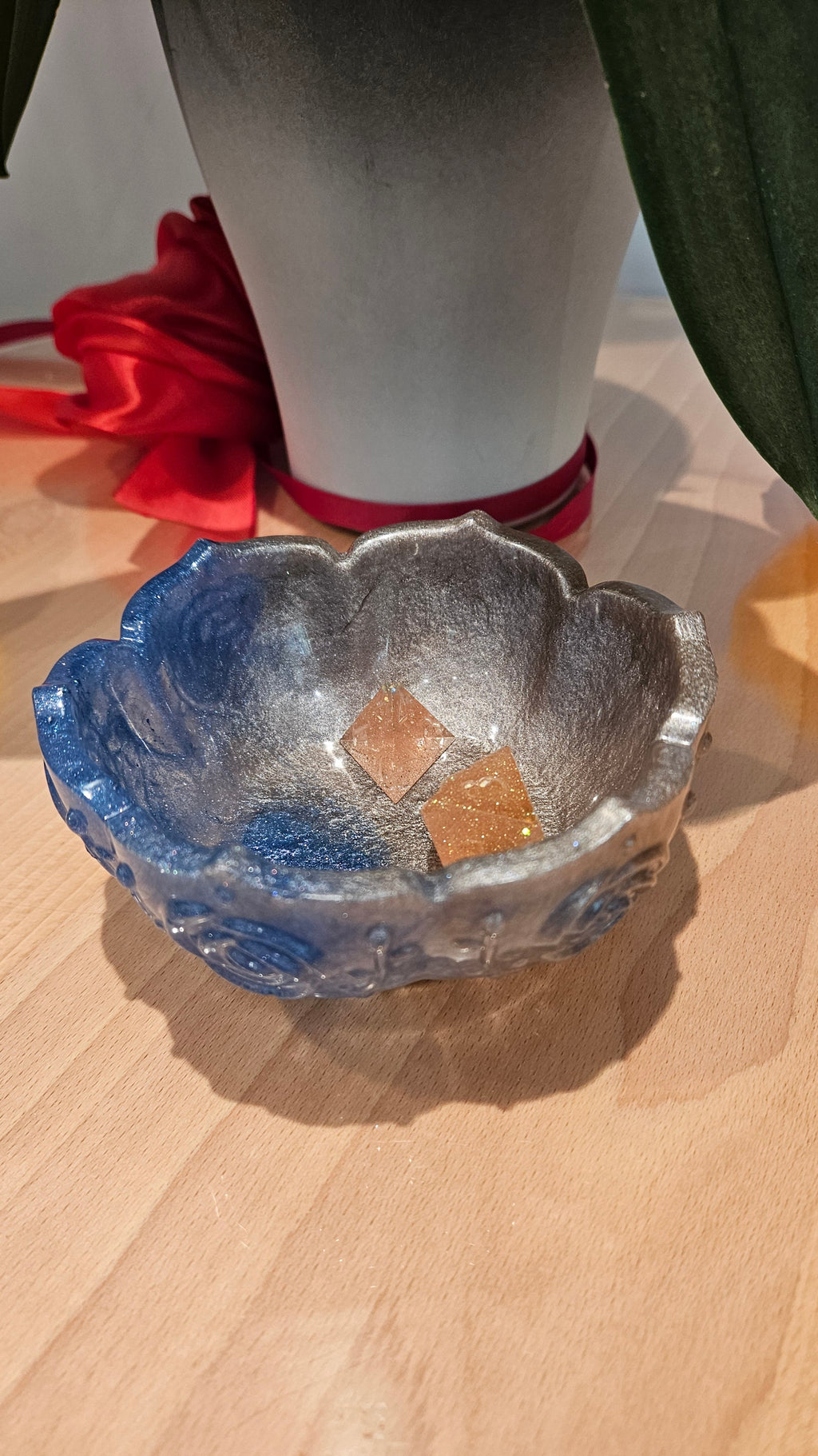 Decorative blue and silver flower-shaped  resin bowl containing dice. On a wooden table. Orchids in the background.