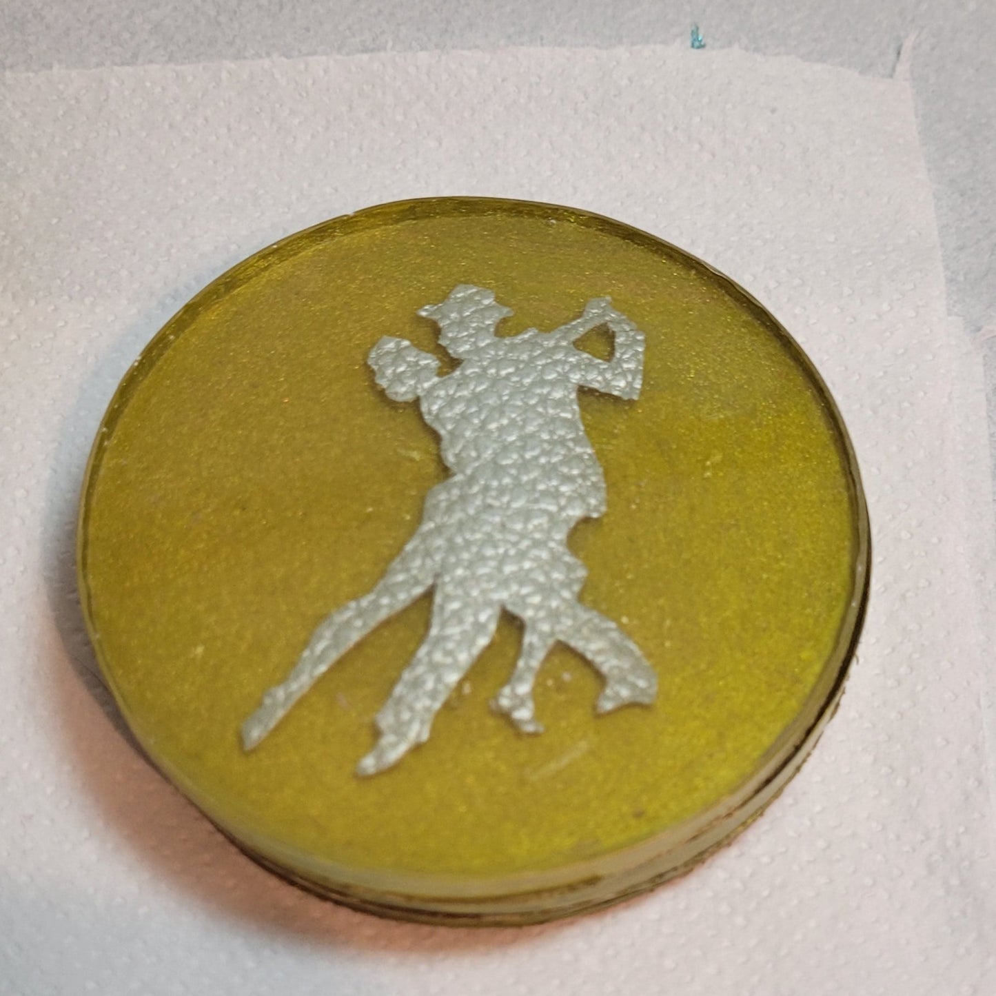 Gold coloured resin circular drinks coaster. Inside is a faux leather pair of Argentine Tango dancers.