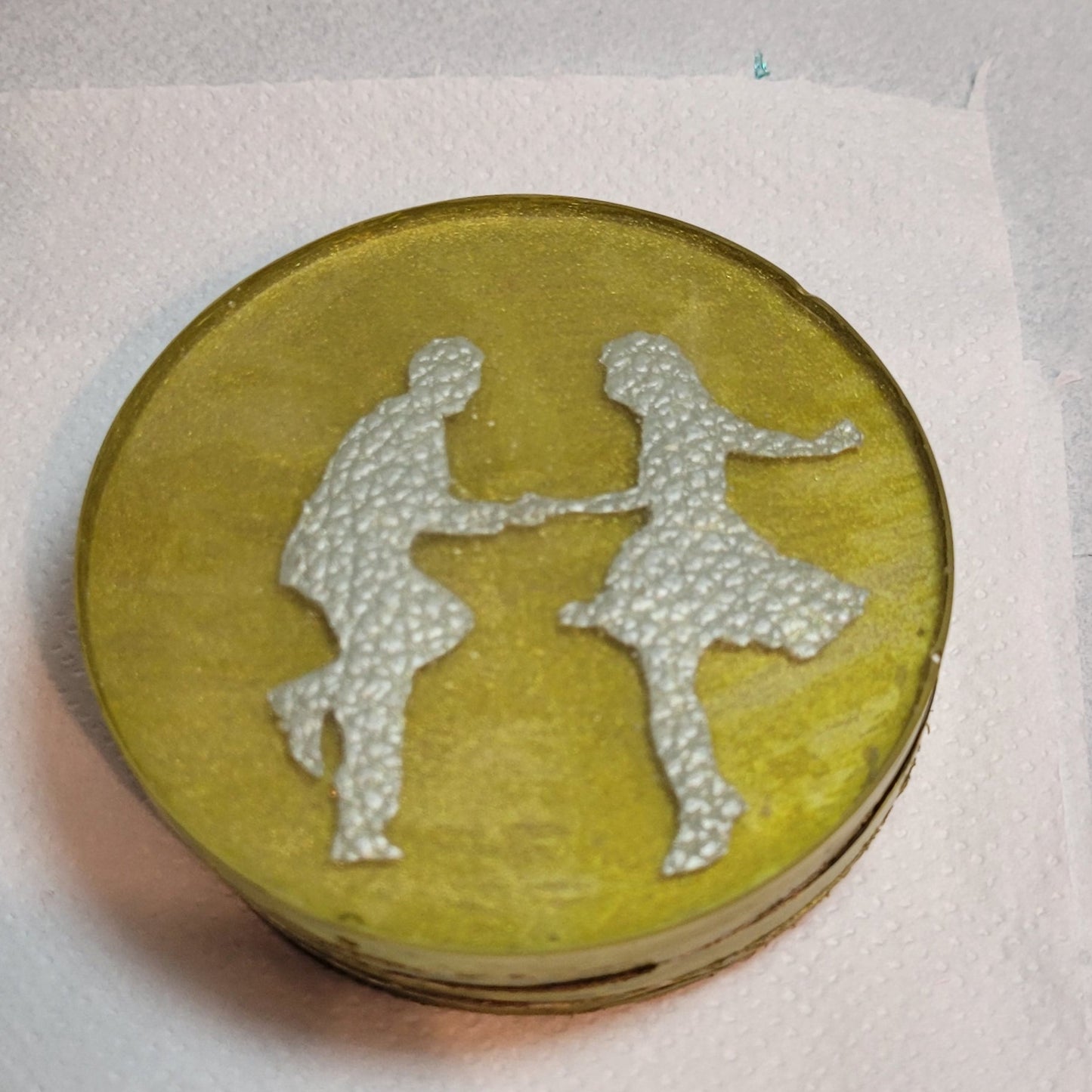 Gold coloured resin circular drinks coaster. Inside is a faux leather pair of rock 'n' roll dancers.