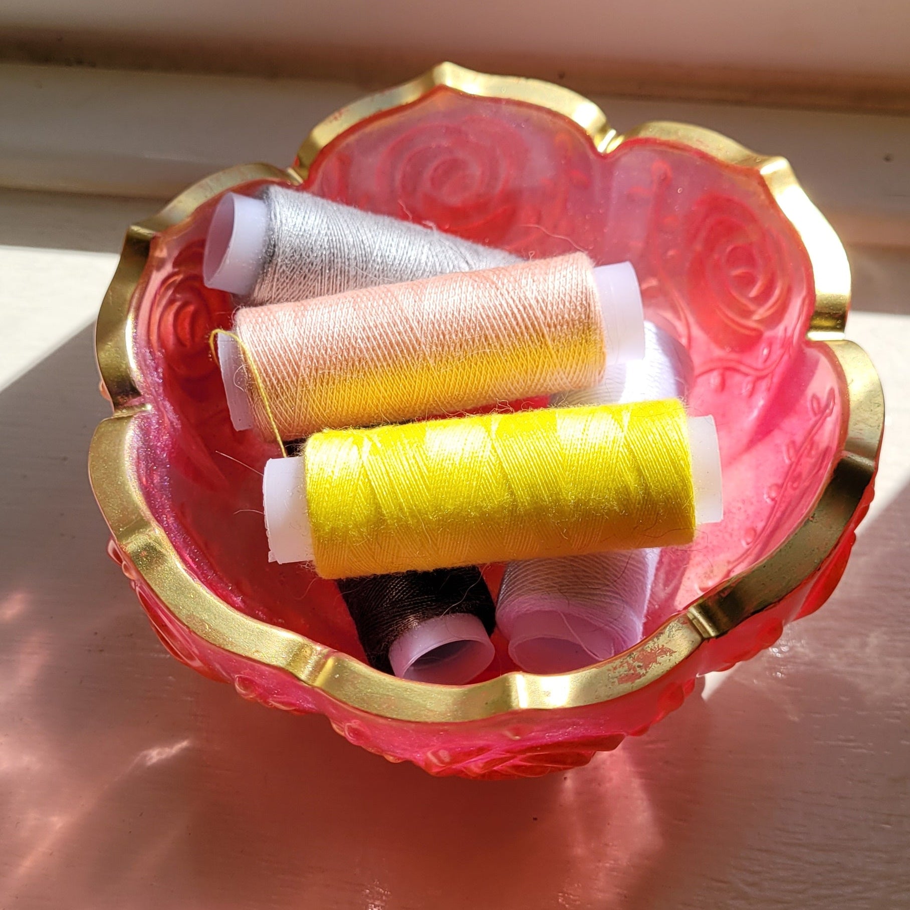 Decorative bowl, pink edged in gold. Displayed holding cotton reels.
