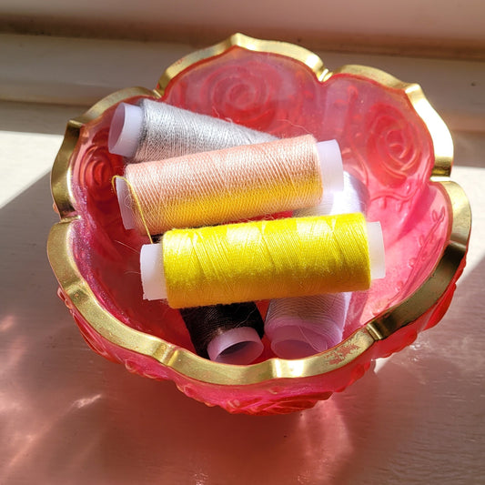 Decorative bowl, pink edged in gold. Displayed holding cotton reels.